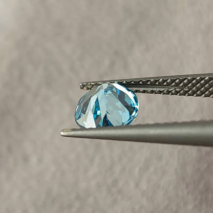 Side view of the blue oval diamond held between tweezers, showing its depth profile.