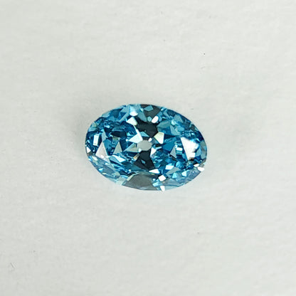 Blue oval diamond face-up on a white surface, showing alternating bright and dark facets.