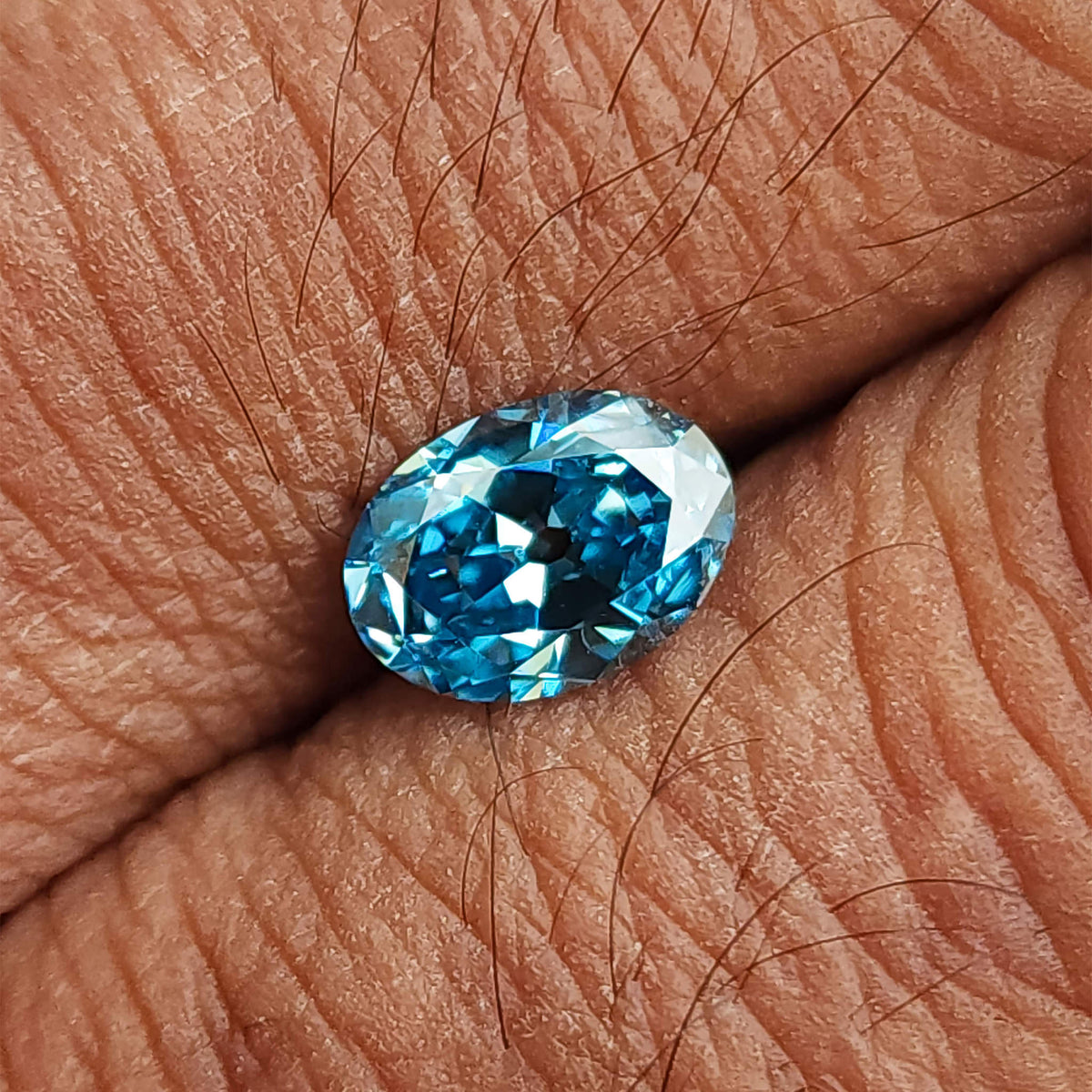 Blue oval diamond resting on a palm, with skin texture providing a scale reference.
