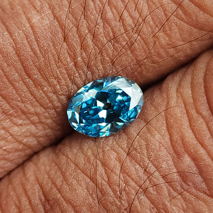 Blue oval diamond resting on a palm, with skin texture providing a scale reference.