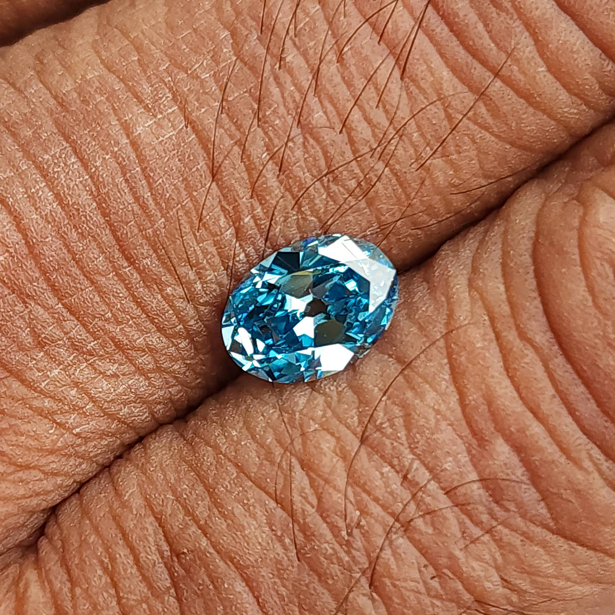 Wider palm view of the blue oval diamond with its full outline visible.