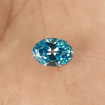 Blue oval diamond resting on a fingertip, viewed face-up.