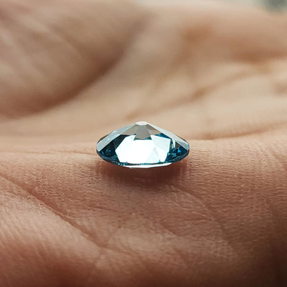 Blue oval diamond resting on its side on a fingertip, showing its depth and reflective facets.