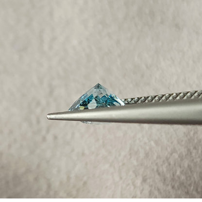 Side profile of the blue diamond held in metal tweezers, showing a pointed pavilion above the jaws; the front jaw partly covers the lower edge.