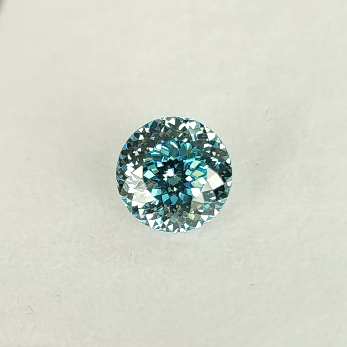 Blue round lab-grown diamond viewed face-up on an off-white pad, with a dark blue center and small bright facets around the circular edge.