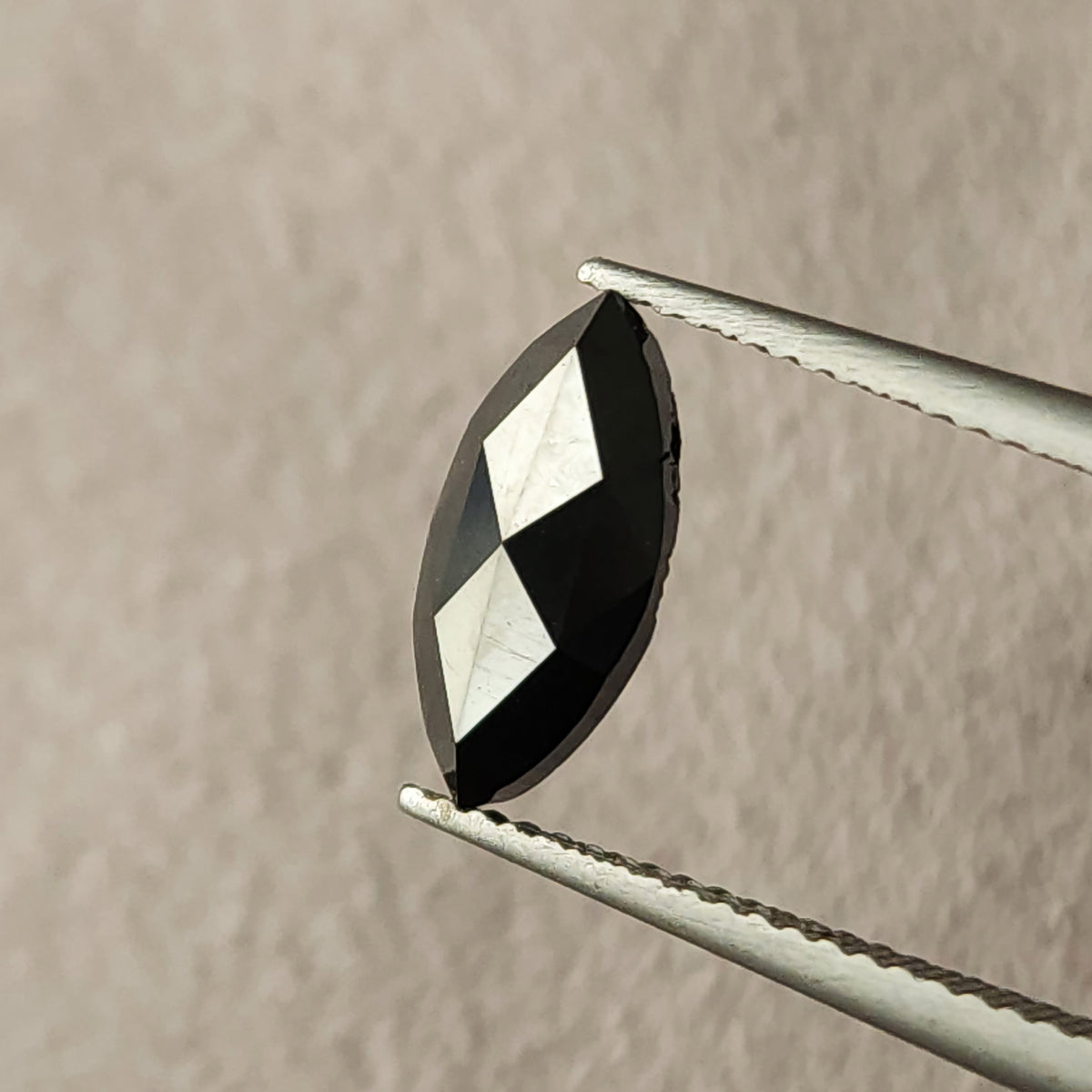 Macro face-up view of a black marquise diamond in tweezers, showing pointed ends, triangular facets and visible surface characteristics.