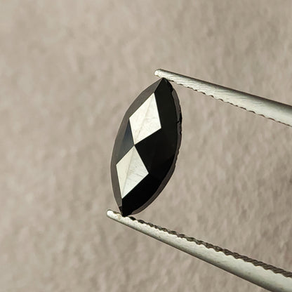 Macro face-up view of a black marquise diamond in tweezers, showing pointed ends, triangular facets and visible surface characteristics.