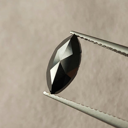 Black marquise rose-cut diamond held face-up in tweezers, with contrasting black and pale triangular facet reflections.