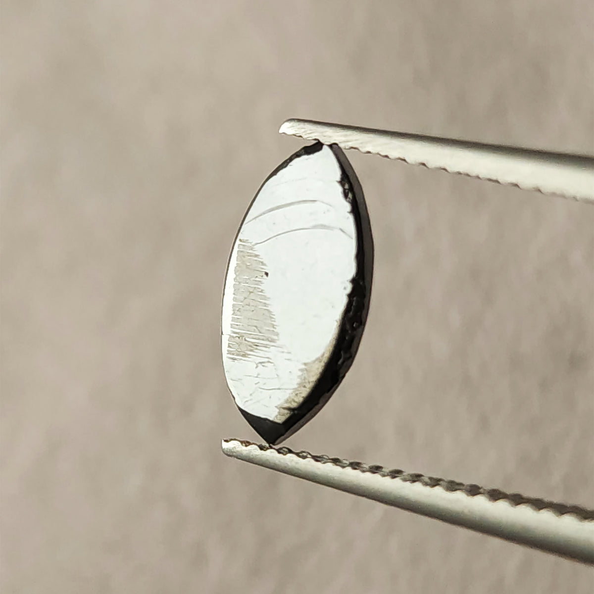 Underside of the marquise diamond held in tweezers, with a broad pale reflection across the flatter surface.