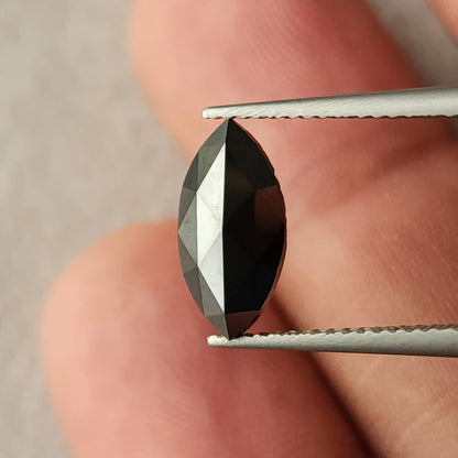 Alternate upright tweezers view of the black marquise diamond near fingers, with bright rose-cut facet reflections.
