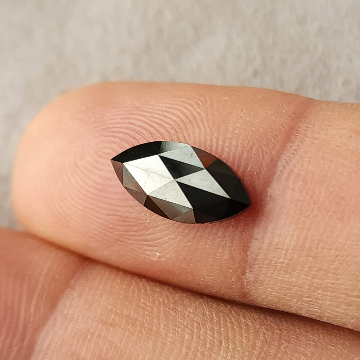 Black marquise rose-cut diamond resting on a fingertip, showing triangular facet reflections and its pointed outline.