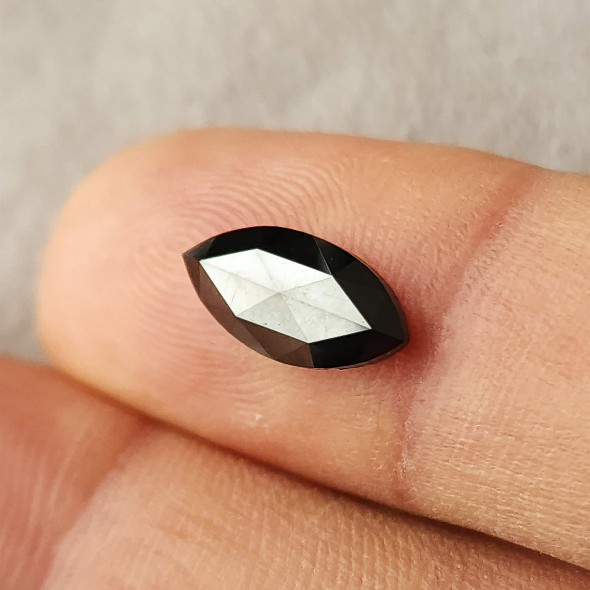 Alternate face-up fingertip view of the black marquise diamond, with a broad bright reflection across the center.