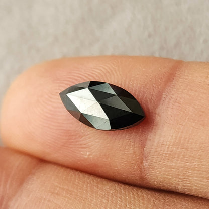 Black marquise rose-cut diamond resting face-up on a fingertip, showing its pointed outline and triangular facet reflections.