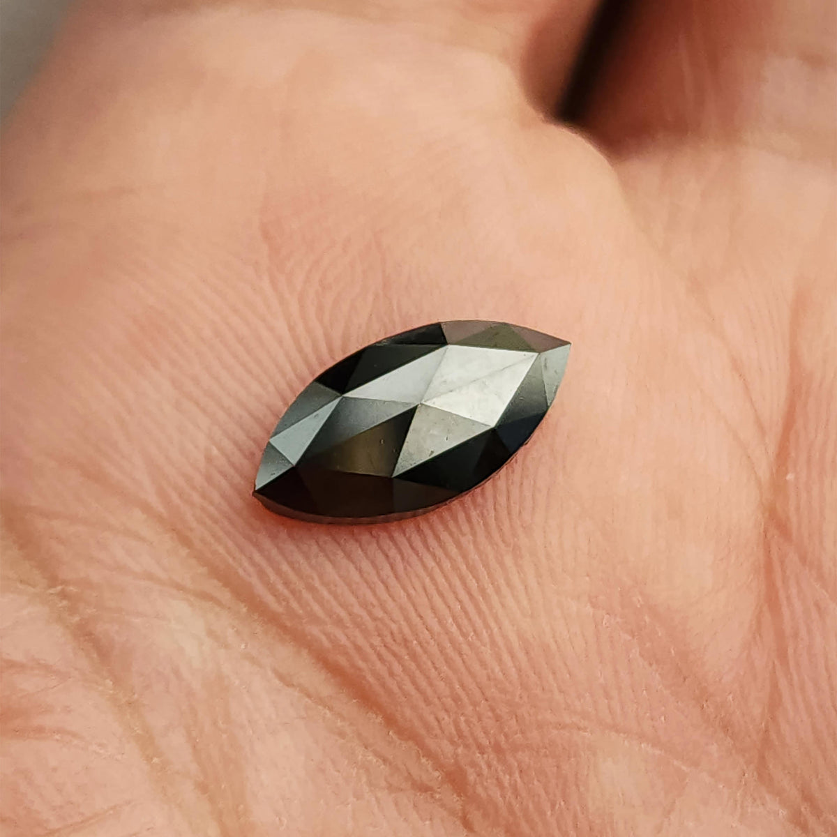 Black marquise diamond lying face-up in a palm, with pale angular reflections across its crown facets.