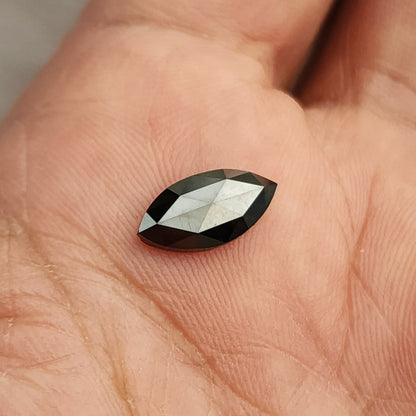 Black marquise rose-cut diamond in a palm at a slightly different angle, with changing bright facet reflections.