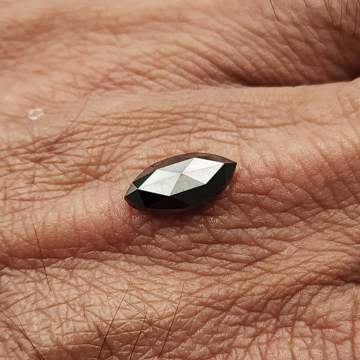 Wider hand-scale view of the black marquise diamond lying on skin, with its pointed ends visible.