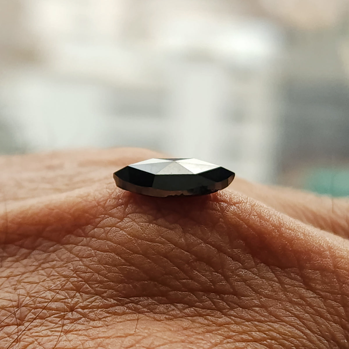 Side-profile view of the black rose-cut marquise diamond on skin, showing its shallow base and raised facets.