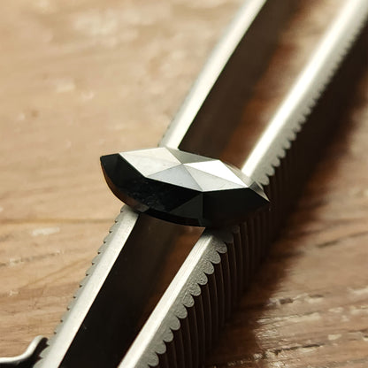 Oblique view of the black marquise diamond across tweezers, showing the crown facets and long outline.