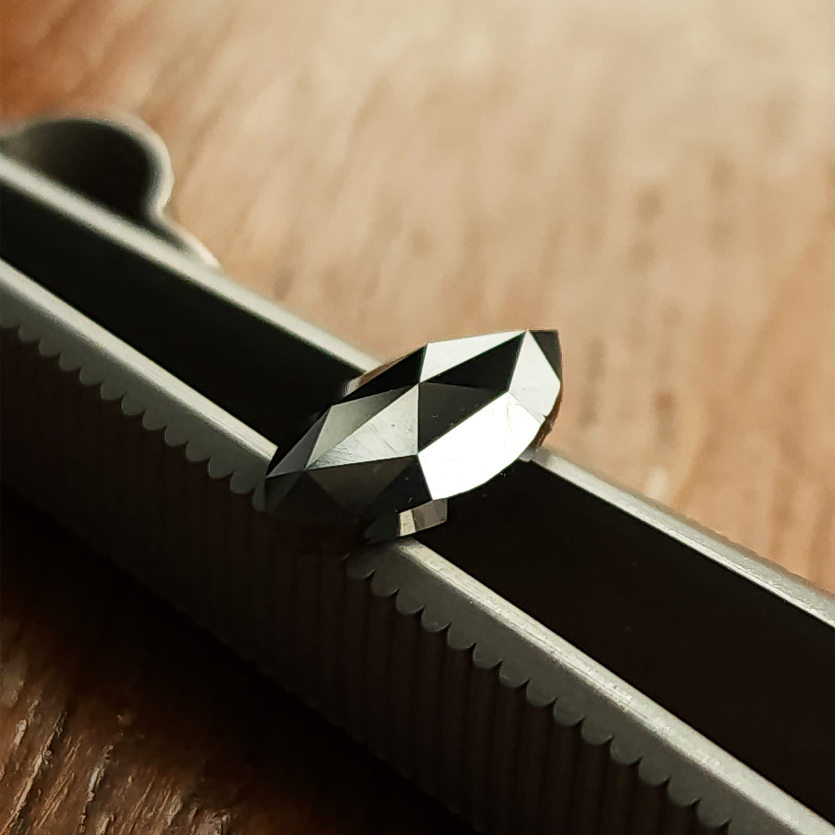 Alternate oblique tweezers view of the black marquise diamond, with bright triangular reflections.