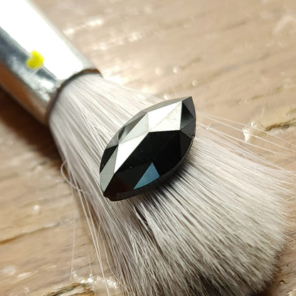Black marquise rose-cut diamond resting on a brush over a wooden surface, viewed obliquely.
