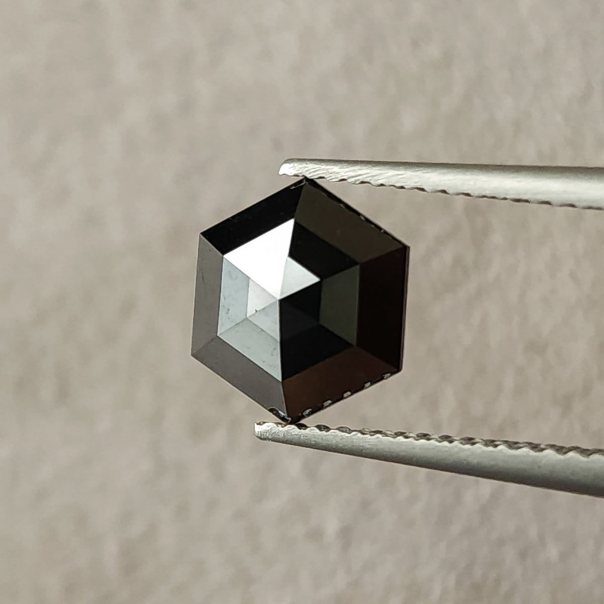 Face-up view of the exact 1.64 ct natural black diamond, showing its rose-cut facets and geometric hexagon outline in tweezers.