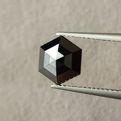 Face-up view of the exact 1.64 ct natural black diamond, showing its rose-cut facets and geometric hexagon outline in tweezers.