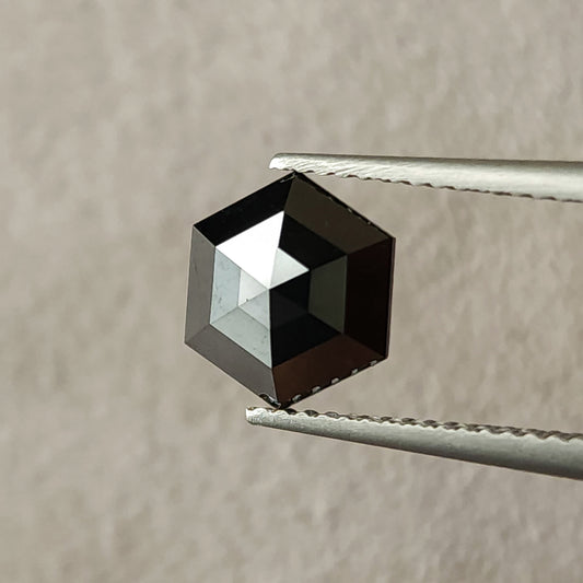 現品の1.64ctの天然ブラックダイヤモンドをピンセットで保持した正面画像。ローズカットのファセットと幾何学的な六角形の輪郭が見える。