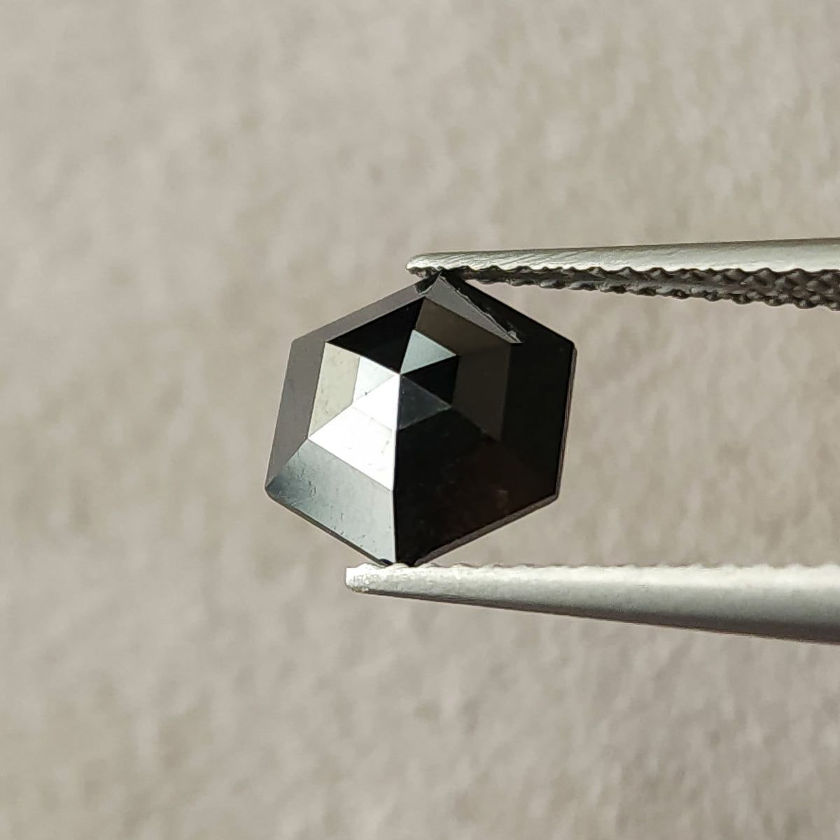 Rotated face-up view of the natural black hexagon diamond in tweezers, showing a different pattern of light and dark facets.