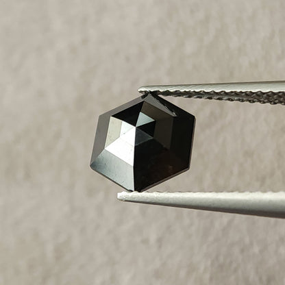 Rotated face-up view of the natural black hexagon diamond in tweezers, showing a different pattern of light and dark facets.
