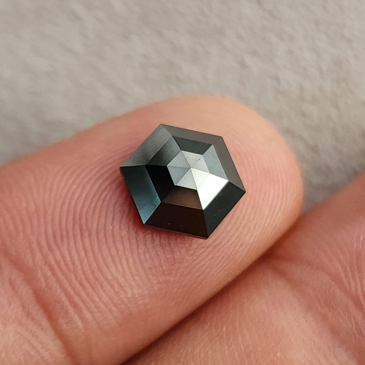 Close face-up view of the rose-cut black hexagon diamond resting on a fingertip, with a bright reflection across the crown.