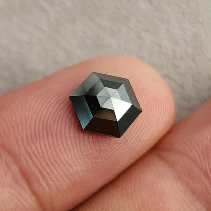 Close face-up view of the rose-cut black hexagon diamond resting on a fingertip, with a bright reflection across the crown.