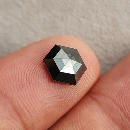 Alternate face-up view of the geometric black diamond on a fingertip, showing its corners and mixed silver-and-black reflections.