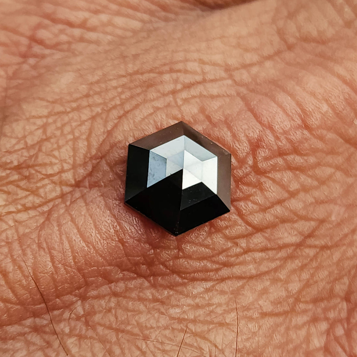 Black hexagon diamond resting on a palm, showing its size relative to the hand and its angular outline.
