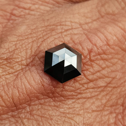 Black hexagon diamond resting on a palm, showing its size relative to the hand and its angular outline.
