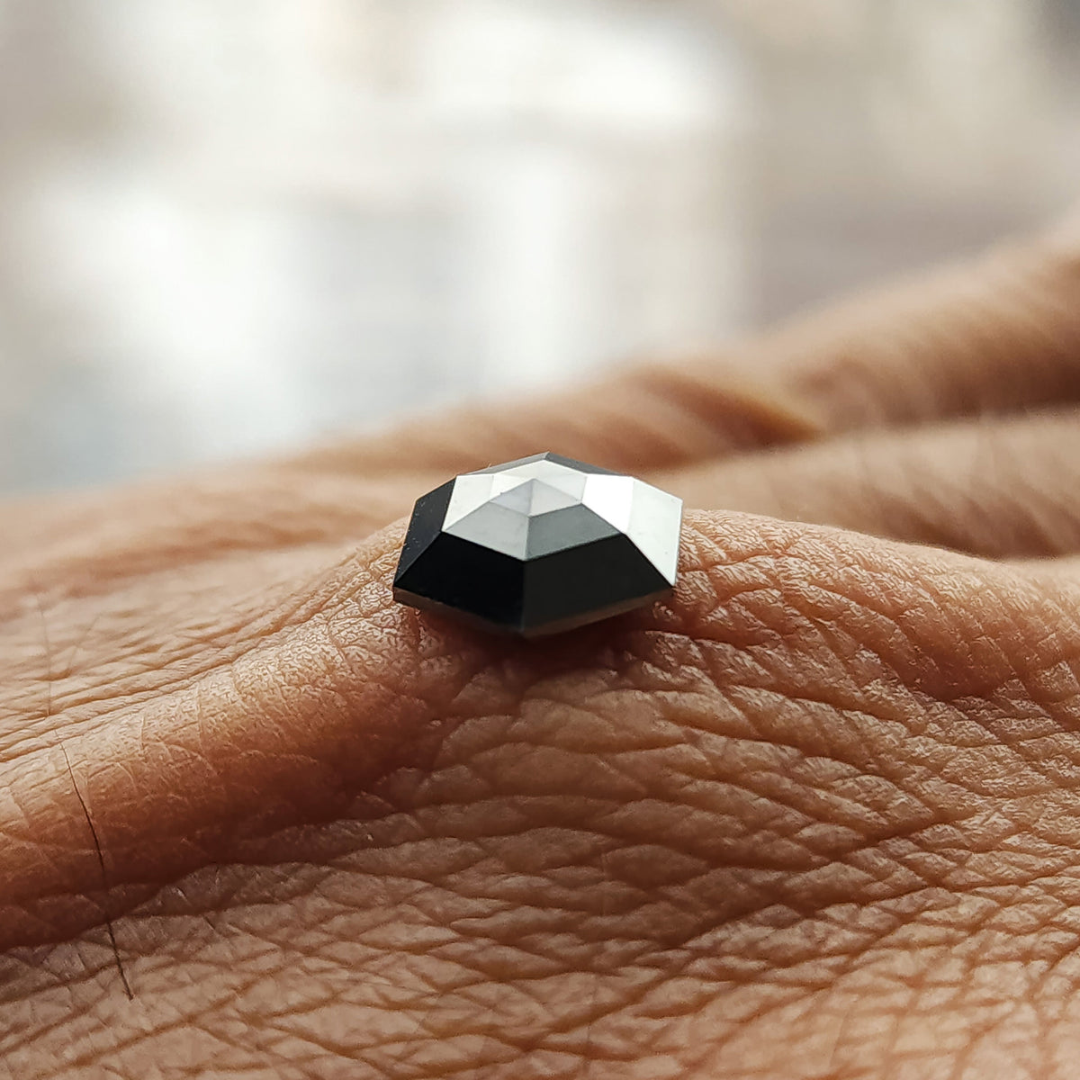 Low side-profile view of the black hexagon diamond resting on a finger, showing its depth and faceted crown.