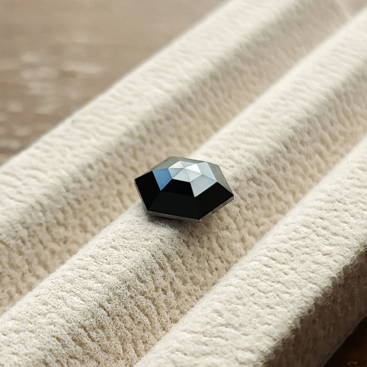 Angled view of the natural black hexagon diamond in a white gem tray, with silver highlights across the rose-cut crown.