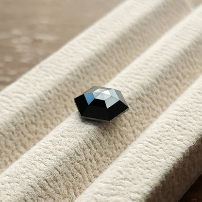 Angled view of the natural black hexagon diamond in a white gem tray, with silver highlights across the rose-cut crown.