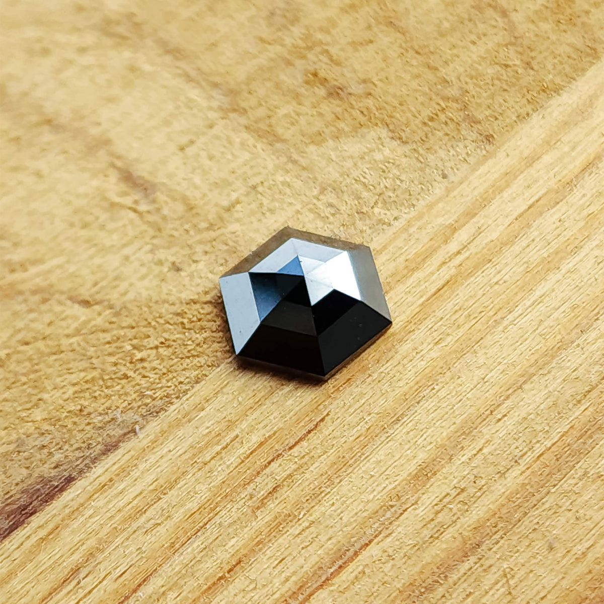 The black hexagon diamond resting on a warm wooden surface, showing its opaque body color and geometric faceting.