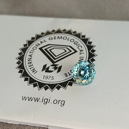 Blue round diamond placed on the printed IGI logo of a laboratory report, with the circular logo and website visible beside the stone.