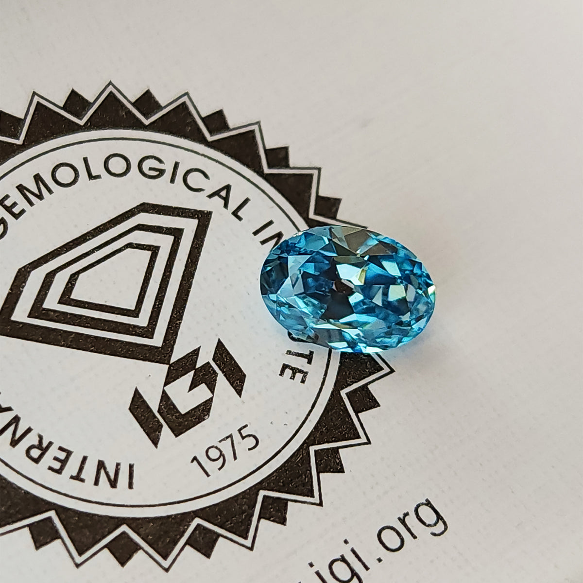 Blue oval diamond photographed over the IGI logo on its report.