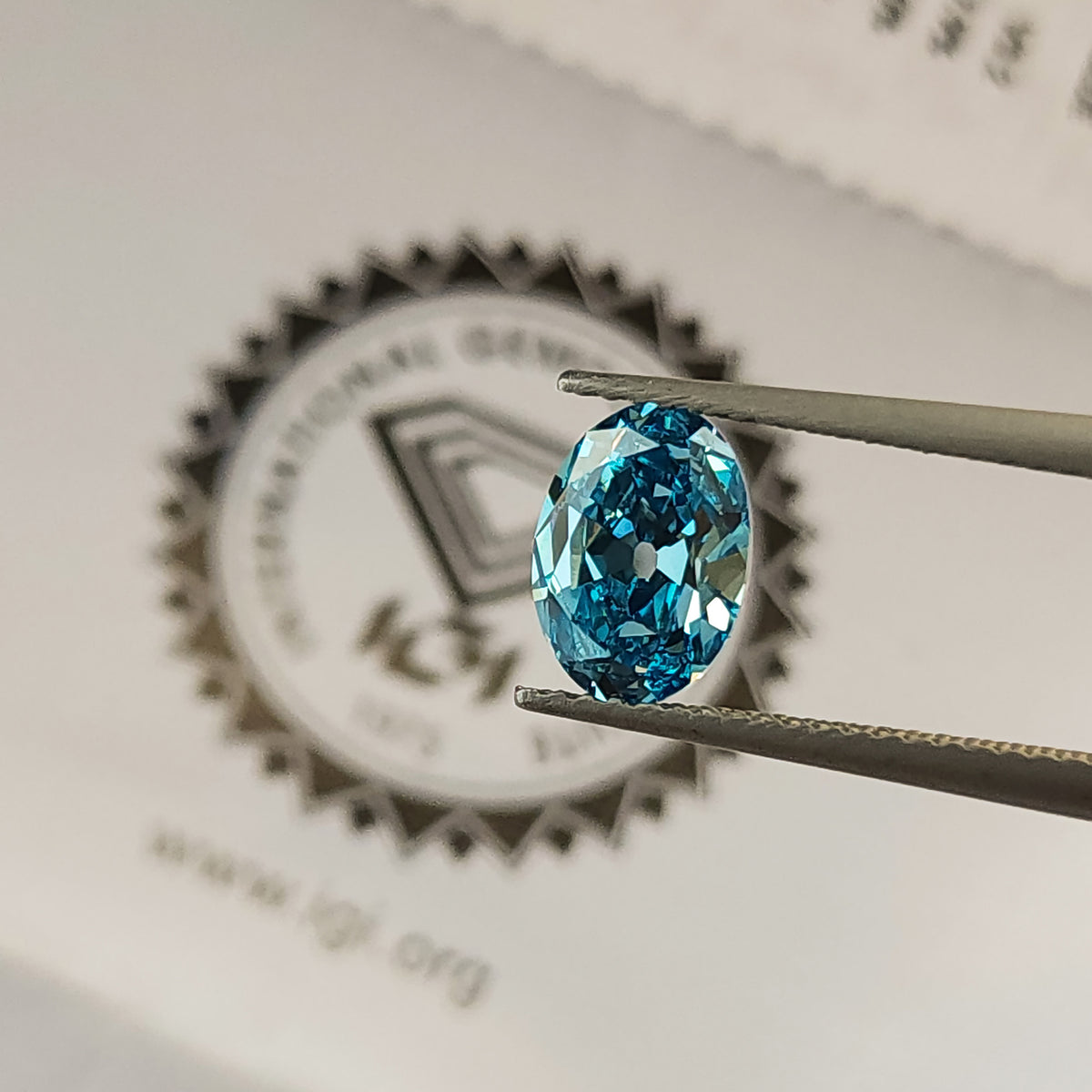 Blue oval diamond held in tweezers above the IGI logo on its report.