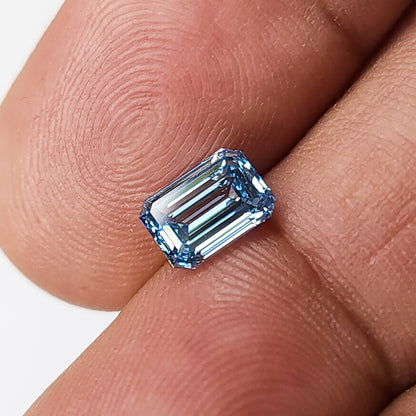 Emerald-cut blue lab-grown diamond lying face-up across fingertips from an alternate angle.