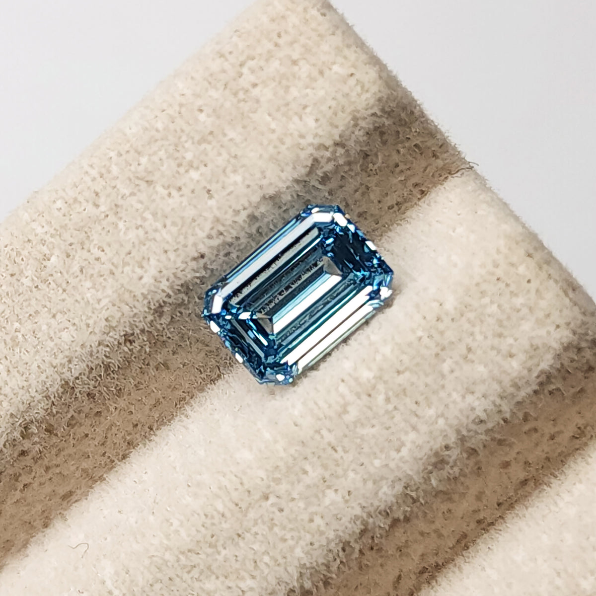 Blue emerald-cut lab-grown diamond resting face-up on a pale textured display ridge.