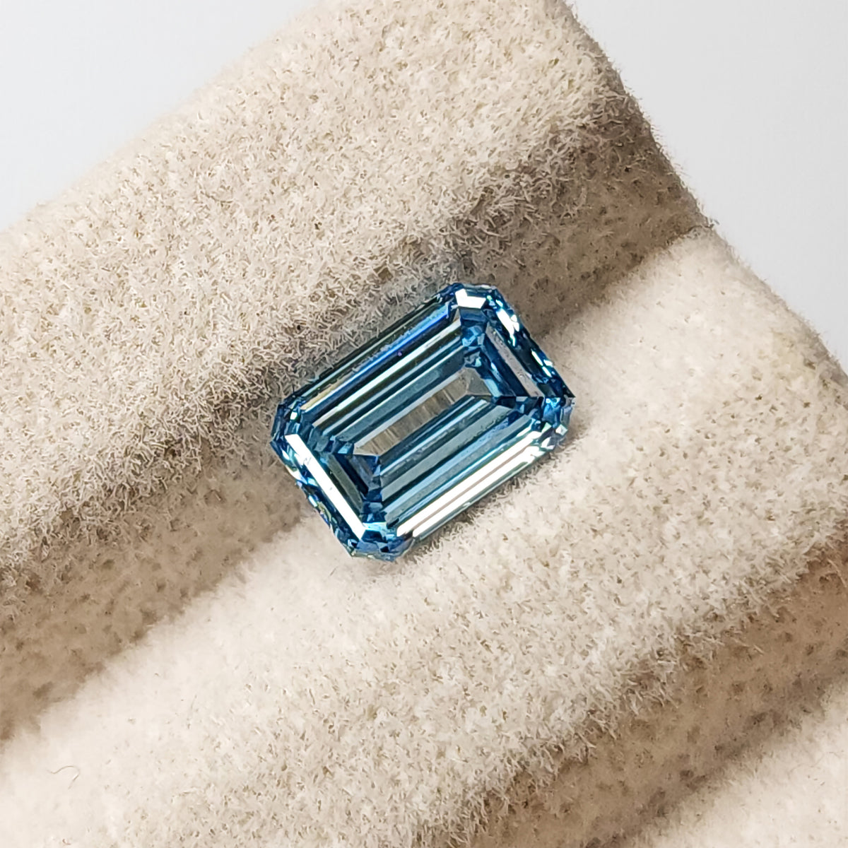 Alternate face-up view of the blue step-cut lab-grown diamond on a pale textured stand.
