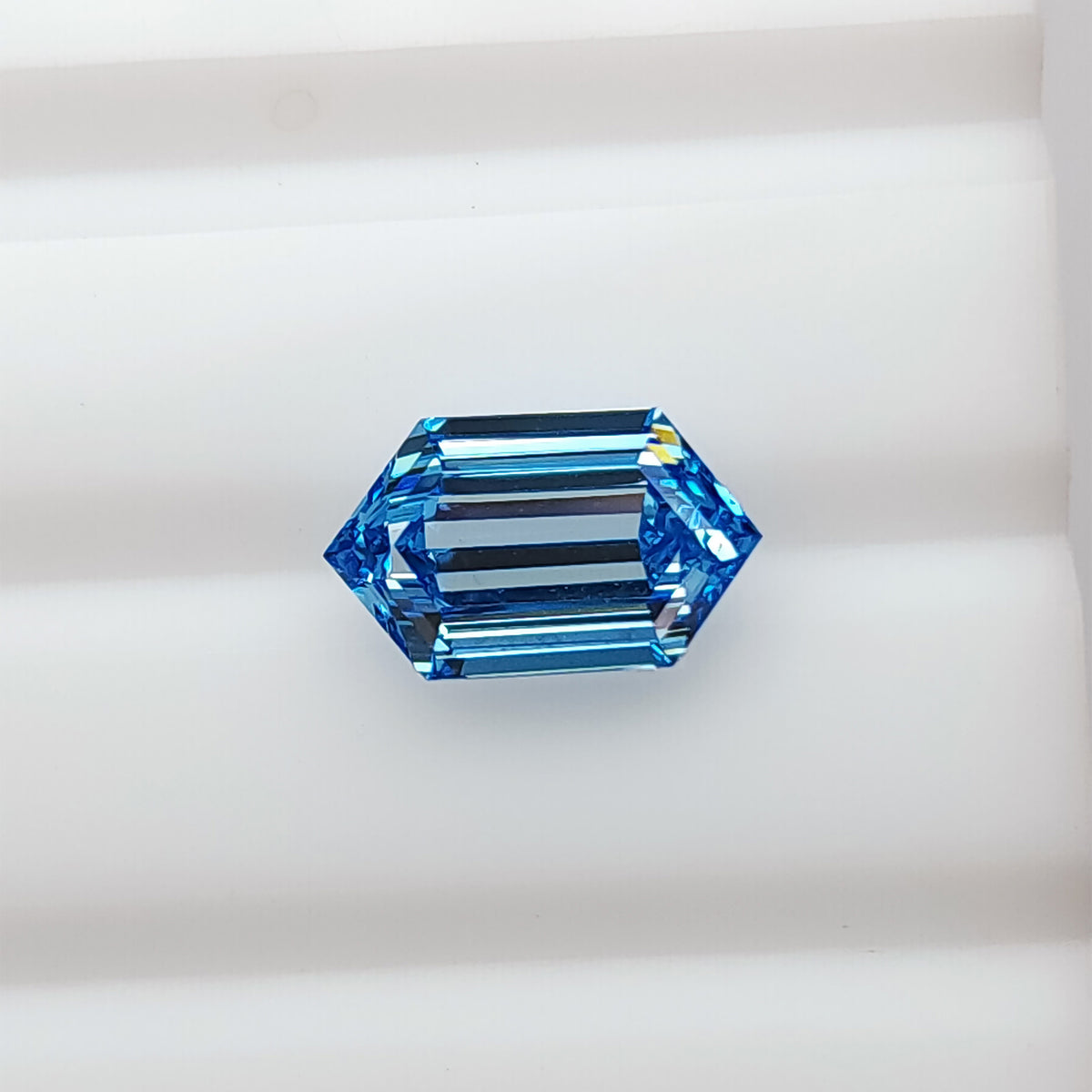 Alternate face-up view of the blue elongated hexagonal diamond on white, with darker central bands and bright blue edges.