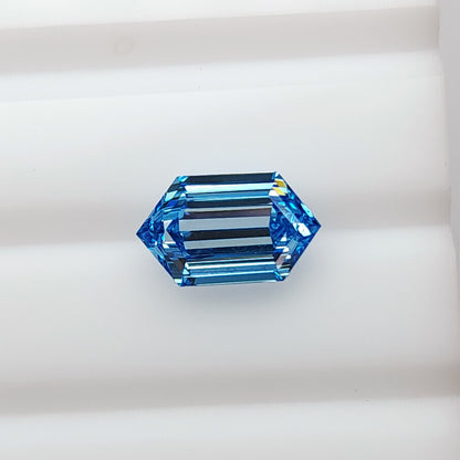 Alternate face-up view of the blue elongated hexagonal diamond on white, with darker central bands and bright blue edges.