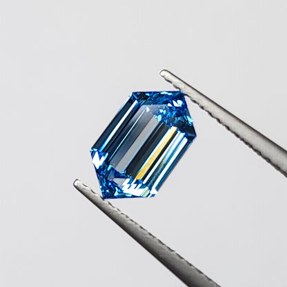 Blue elongated hexagonal diamond held face-up in tweezers, showing its six-sided outline and step facets.