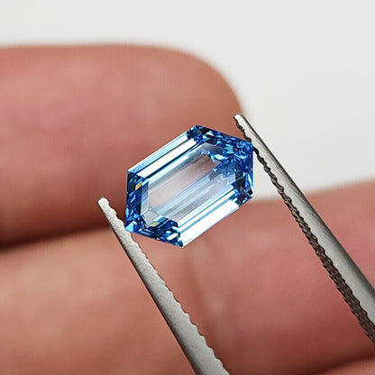 Alternate tweezers view of the blue hexagonal diamond near a fingertip, with bright pale reflections across the center.