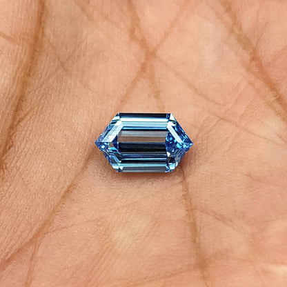 Blue hexagonal step-cut diamond viewed face-up in a palm, showing its outline and darker center bands.
