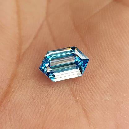 Blue hexagonal diamond in a palm at a different angle, with pale reflections across its step-cut center.